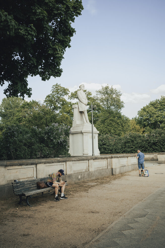 Ein Mann steht vor dem Denkmal des preußischen Feldherrn Molte, ein Mann sitzt auf einer Bank und schaut auf sein Smartphone