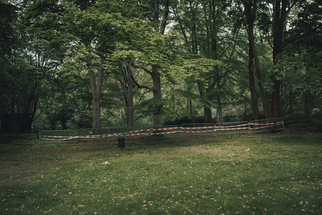 Ein Absperrgitter mit rotem Band steht auf einer Wiese vor Bäumen und Büsche