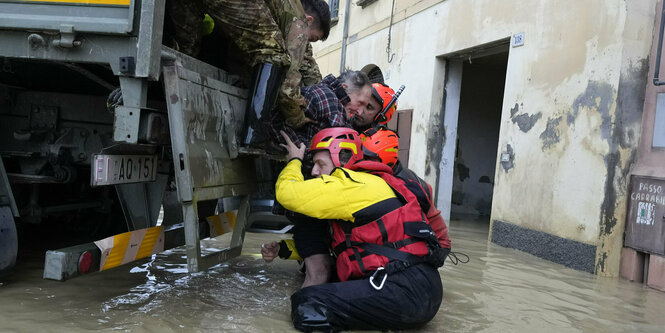 Feuerwehrleute stehen bis zur Hüfte im Wasser und schieben einen Mann auf die Ladefläche eines Lastwagens