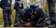 Behelmte Polizisten fixieren einen Menschen am Boden
