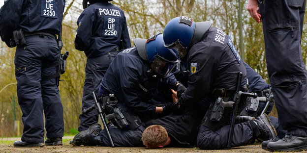 Behelmte Polizisten fixieren einen Menschen am Boden