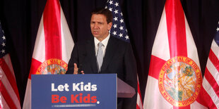 Ron DeSantis steht an einem Rednerpult mit der Aufschrift "Let kids be kids"