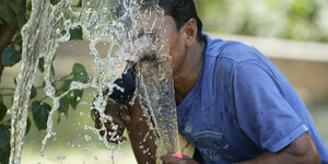 Ein Mann in Indien trinkt Wasser aus einem Gartenschlauch