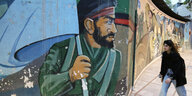 Eine Straßenszene mit Wandbild eines Revolutionswächters und eine junge Frau ohne Kopftuch