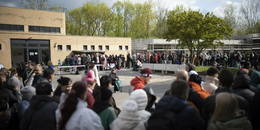 Menschenmassen stehen in einem Schulhof Schlange