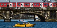 Eine rote S-Bahn auf einer Brücke über einem Gewäser mit kleinen Booten