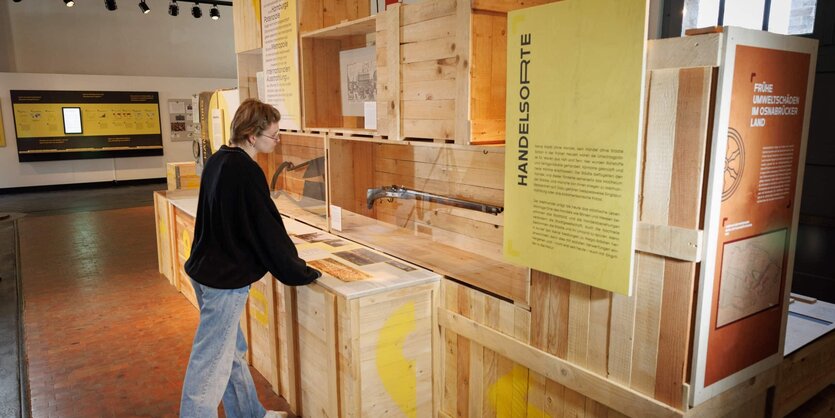 Eine Besucherin steht vor einem Holzregal mit Exponaten.