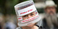 Ein Demonstrant läuft mit einem auf den Kopf gesetzten Plastikeimer, beschriftet mit «Absolut sicher gegen das Verdummungsvirus»
