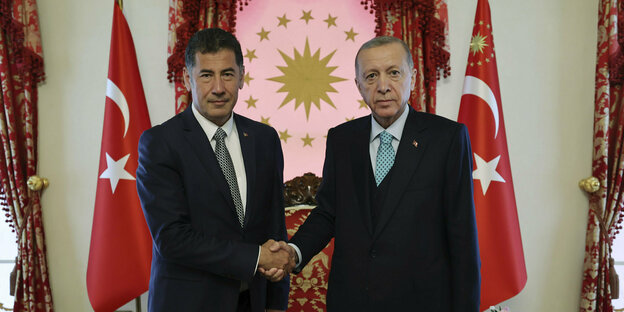 Zwei Männer geben sich die Hand vor zwei türkischen Flaggen