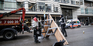 Mitarbeiter eines Planungsbüros tragen Sitzelemente für Bänke auf der Friedrichstrasse von einem Kran.