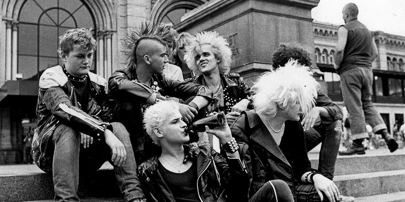 Eine Gruppe Punks sitzt vor dem Bahnhof in Hannover, einer trinkt aus einer Flasche.