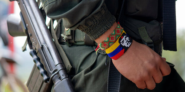 Ein Mann mit Uniform und Waffe. Er trägt ein Armband mit den kolumbianischen Farben gelb- blau-rot darauf ist Guevara zu sehen