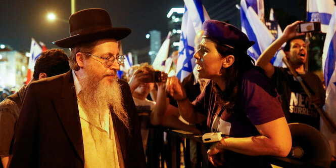 Ein Ultraorthodoxer Mann wird von einer Frau bei einer Demo angeschrien