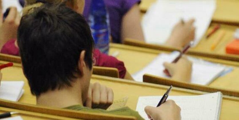 Einige Studierende von hinten fotografiert sitzen in einer Vorlesung und machen sich Notizen.