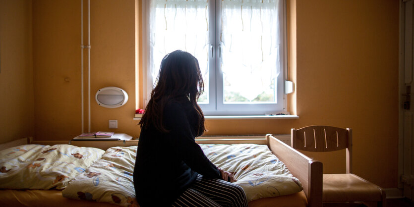 Eine Frau sitzt auf einem Bett und schaut aus dem Fenster.