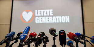 Aufgereite Mikrofone, im Hintergrund das Logo der Letzten Generation