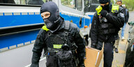 Zwei Polizisten tragen einen Karton mit beschlagnahmten Gegenständen