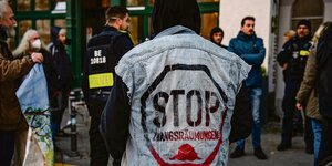 Ein Mensch ist von hinten zu sehen. Auf seiner Jeans-Weste steht "STOP ZWANGSRÄUMUNGEN". Im Hintergrund stehen Polizisten und andere Demonstranten.