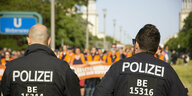 Zwei Polizisten, von hinten fotografiert, beobachten eine Demo der Letzten Generation am 26. Mai 2023 in Berlin