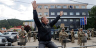 Ein Mann gestikuliert vor einem Gebäude, das von Soldaten bewacht wird