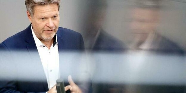Wirtschaftsminister Habeck hinter einer spiegelnden Glasscheibe die einen milchigen Streifen über seine Brust legt