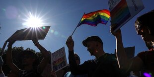 Menschen protestieren, eine hält eine Regenbogenfahne in den Händen