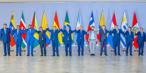 Zwölf Männer stehen Hand in Hand vor zwölf Landesflaggen