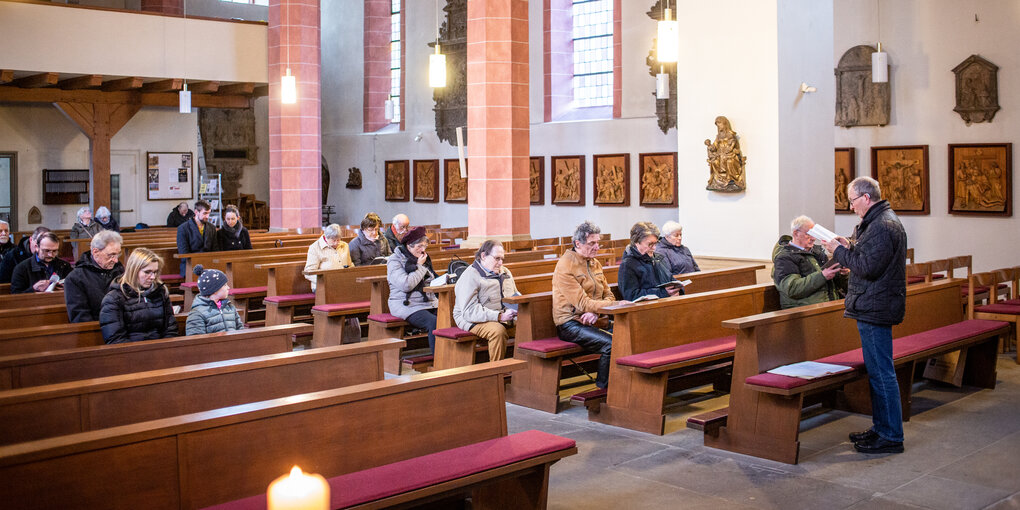 Ein Mann mit einem Buch steht vor Menschen in Kirchenbanken