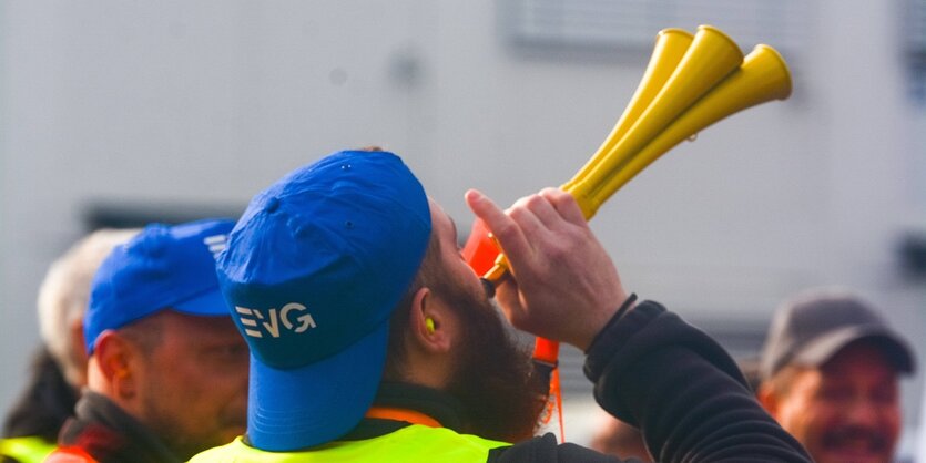 Ein mann mit einer blauen Kappe, auf der der SChriftzug "EVG" zu lesen ist, bläst in eine Tröte