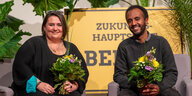 Das Foto zeigt die beiden Berliner Grünen-Landesvorsitzenden Susanne Mertens und Philmon Ghirmai mit Blumensträußen in den Händen