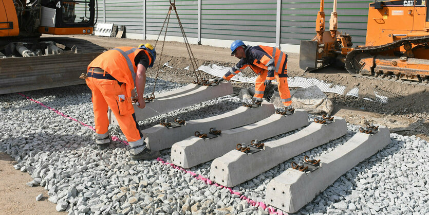 Arbeiter verlegen mit Hilfe eines Raupenbaggers Betonschwellen