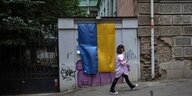 Eine Frau geht an einer Mauer vorbei, an der eine ukrainische Fahne hängt