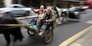 2 Männer und ein Kind rasen mit einer Kutsche eine Straße entlang