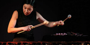 Taiko Saito steht auf eine Bühne, vor ihr steht ein Vibraphon. Sie schaut konzentriert zu Boden und spielt das Instrument mit vier Schlägeln.