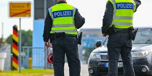 Zwei Polizisten an einer Brücke, im Hintergrund ein schwarz-rot-goldener Grenzpfahl