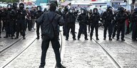 Ein schwarz gekleideter Mensch steht einer Reihe von Polizist:innen in Schutzausrüstung gegenüber
