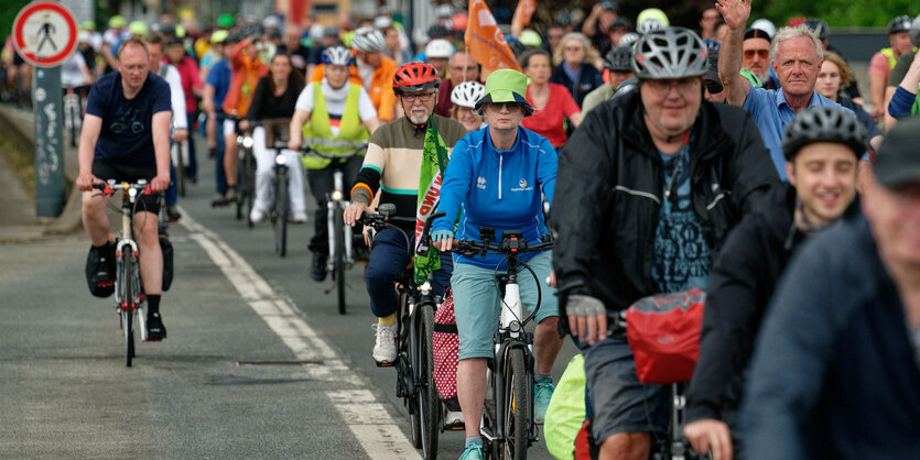 AUf einer Landstraße fahren viele Radfahrer auf einer Radfahrdemontration. Wir stehen am Straßenrand und schauen zu.