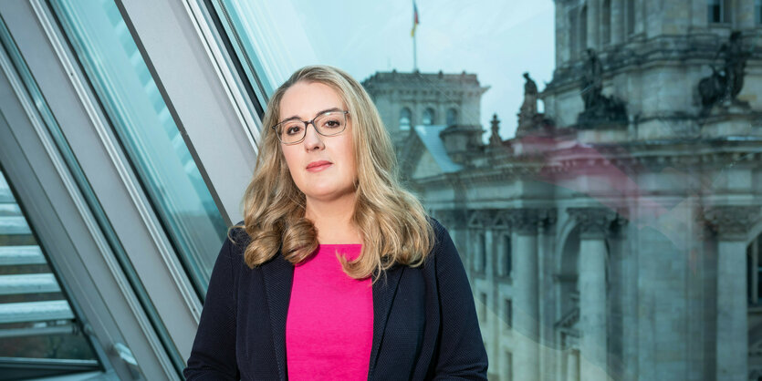 Frau im Blazer vor Panoramafenster mit Blick auf die Reichstagskuppel