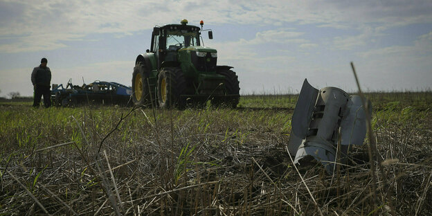 Traktor und Bauer auf einem Feld, im Vordergrund Trümer einer Rakete