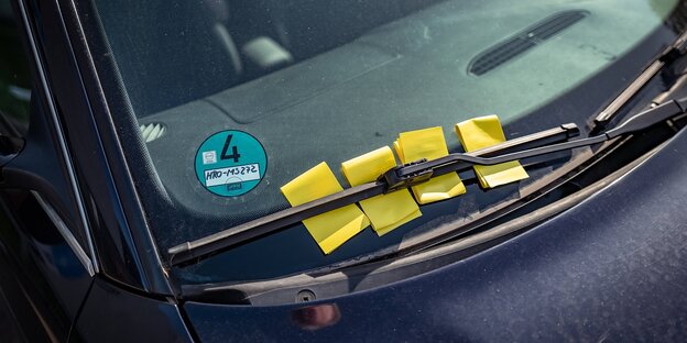 Gelbe Zettel klemmen hinter einem Scheibenwischer eines Autos