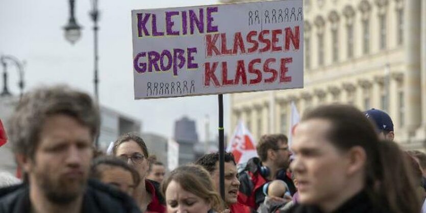 Gesichter von Demonstrant*innen sind zu sehen, über ihnen wird ein Schild hochgehalten. Darauf ist zu lesen: "Kleine Klasse, große Klasse".