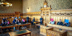 Saal im Landgericht Bremen, die vier Angeklagten sitzen mit Mappen vor den Gesichtern neben Anwälten