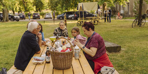 Eine Menschengruppe sitzt an einem Holztisch in einem Garten und isst