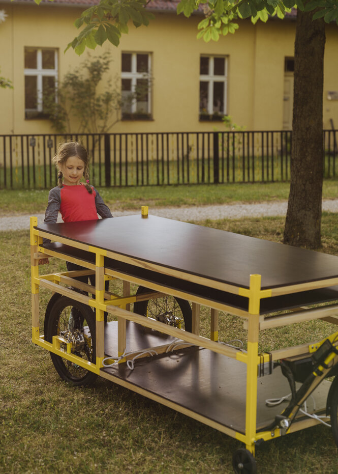 Ein Kind sitzt auf einem E-Fahrradanhänger der mobil als Tafel aufgebaut werden kann