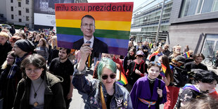 Eine Menschenmasse bewegt sich. Darunter ist eine Frau, die ein Plakat auf dem Edgars Rinkevics in Regenbogenfarben zu sehen ist, hält