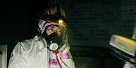 Ein Arbeiter des Reaktors in Fukushima sitzt in einem Schutzanzug am Schreibtisch und telefoniert