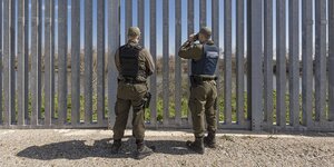Zwei Grenzschützer blicken durch einen Zaun aus Beton