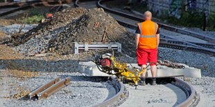 Ein Arbeiter in orangefarbener Arbeitskleidung steht an einer Gleisbaustelle