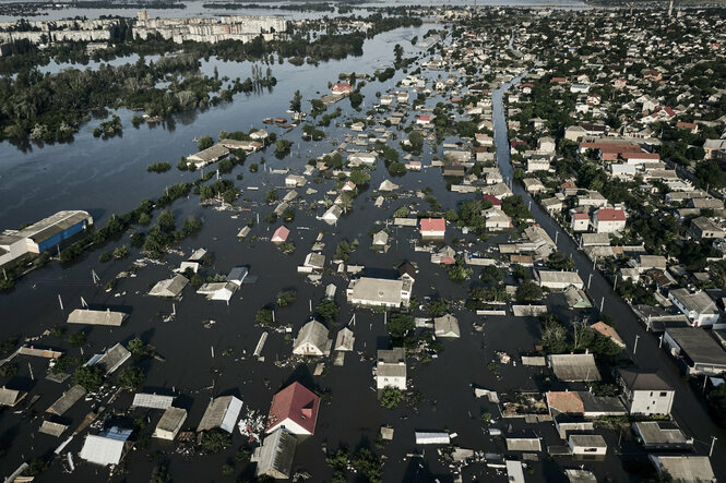 Luftaufnahme einer überschwemmten Stadt. Das Wasser steht bis zu den Dächern der Wohnhäuser.