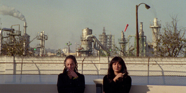 Zwei Frauen sitzen vor einer Ölraffinerie